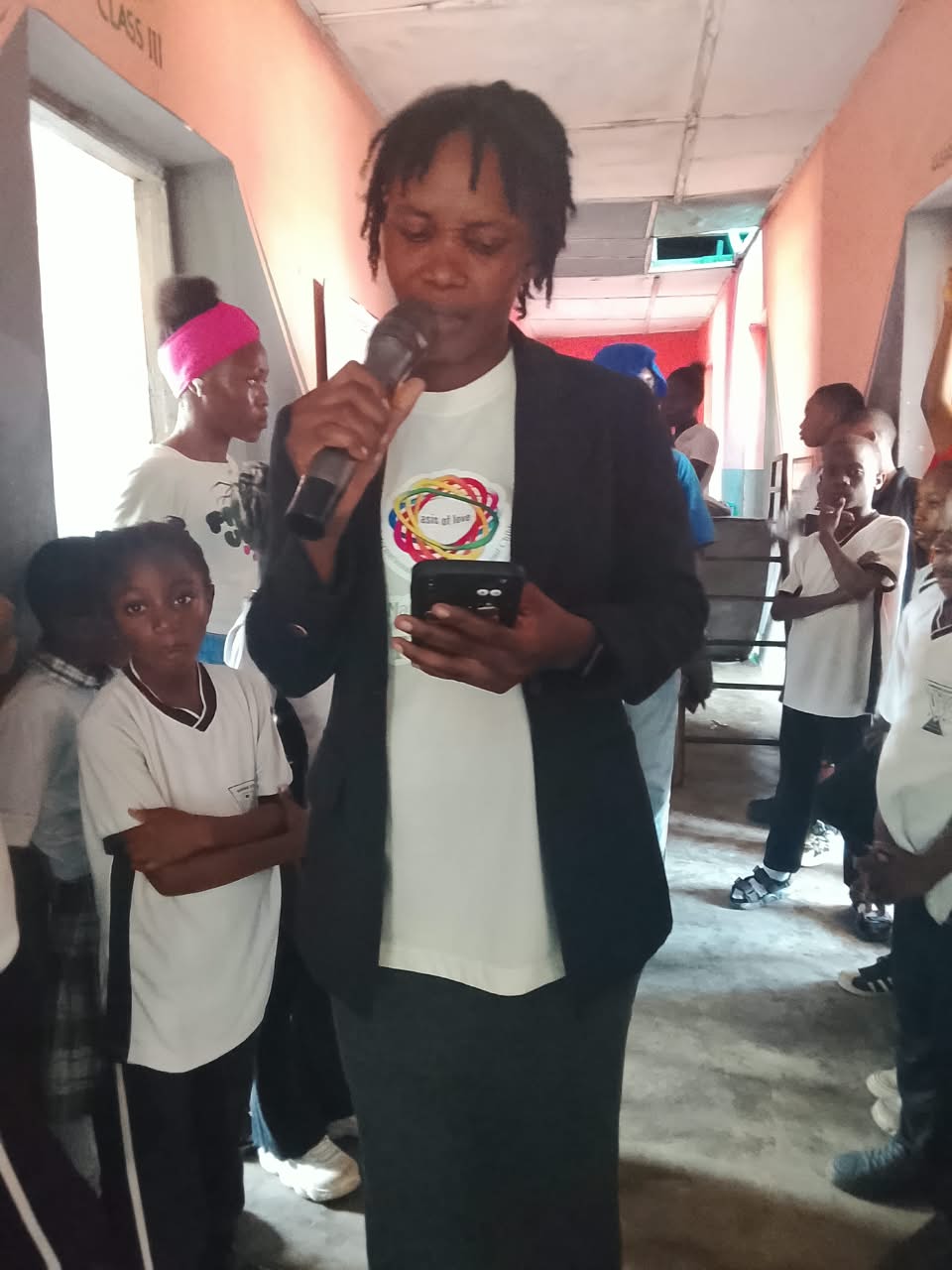 Margareth Oluwatomiwa, OLIC facilitator, speaking into a microphone to students gathered in a school corridor during the seminar